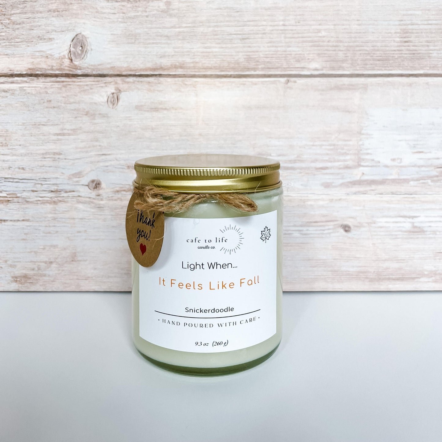 Candle with gold top screwed on. Label says "Light When... It Feels Like Fall" in orange font.