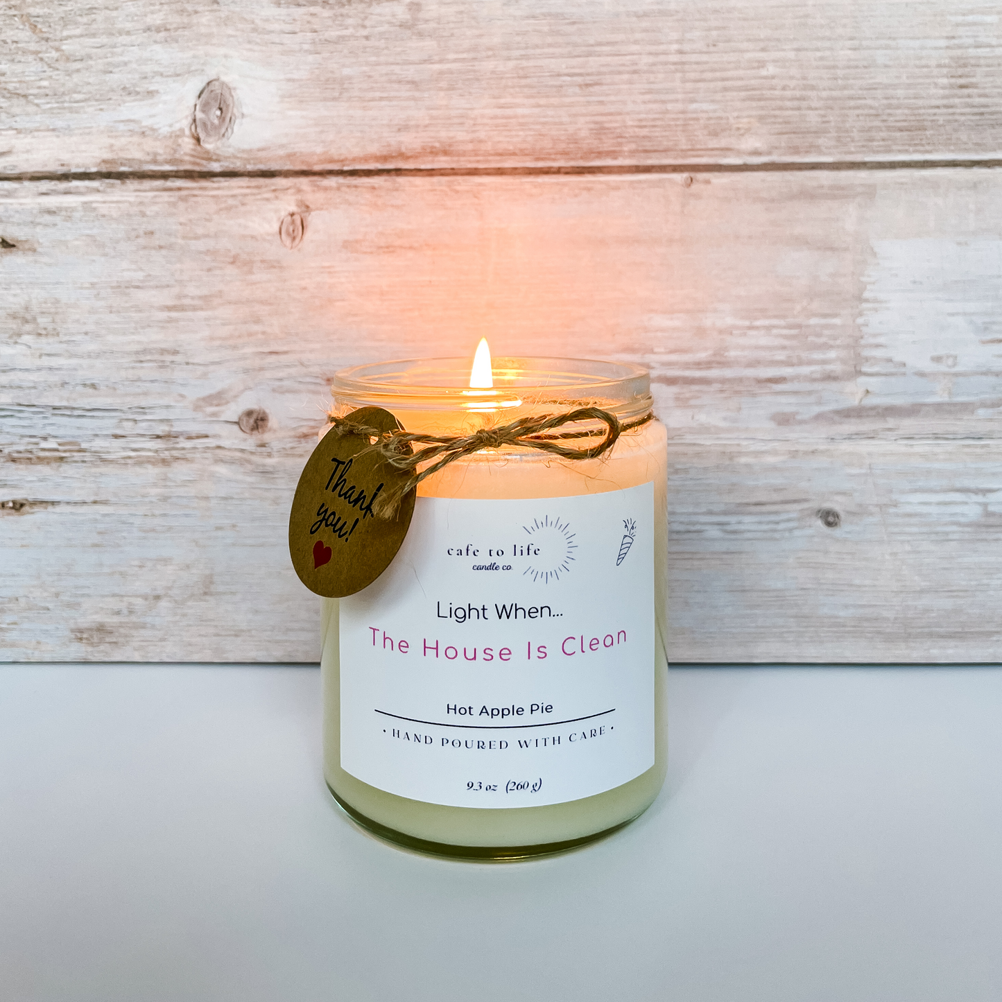 Candle with flame. Twine tied in a bow around candle. Label says, "Light When... The House Is Clean"