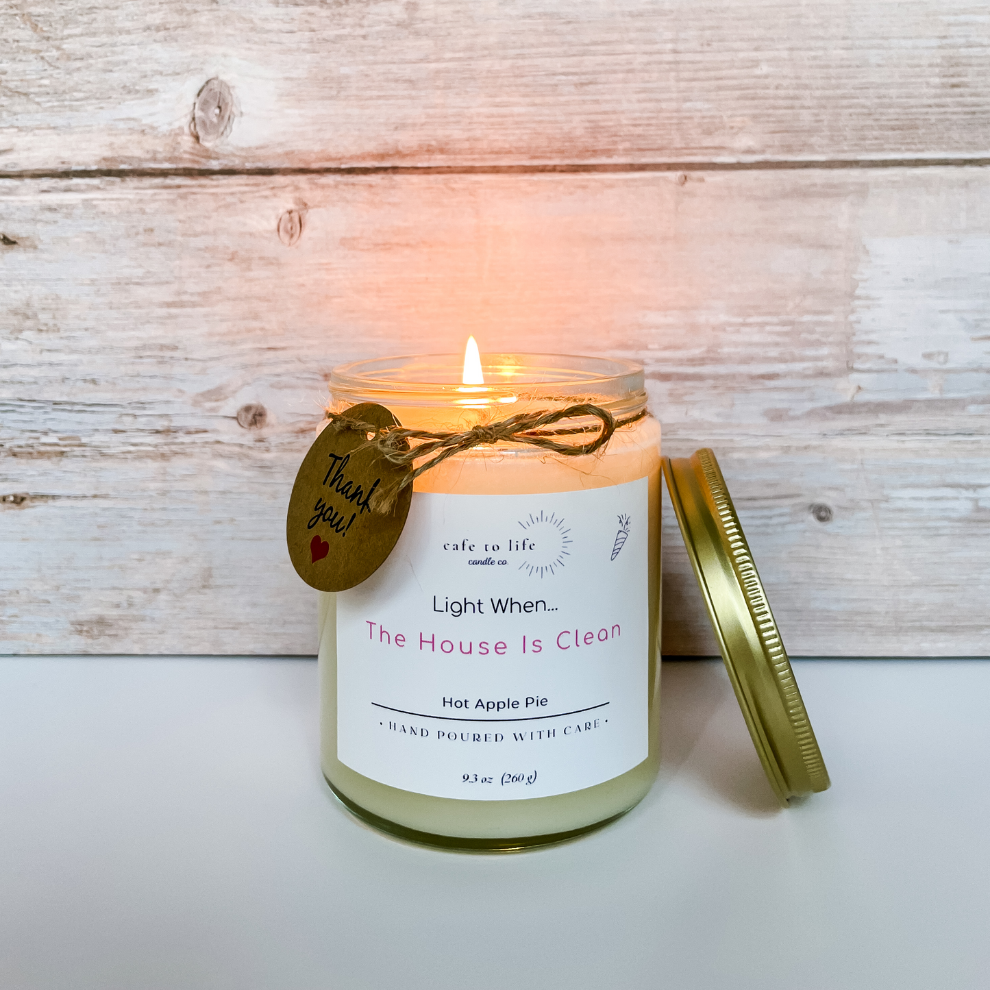 Candle with flame, twine tied in a bow, and thank you tag. Label says, "Light When... The House Is Clean"