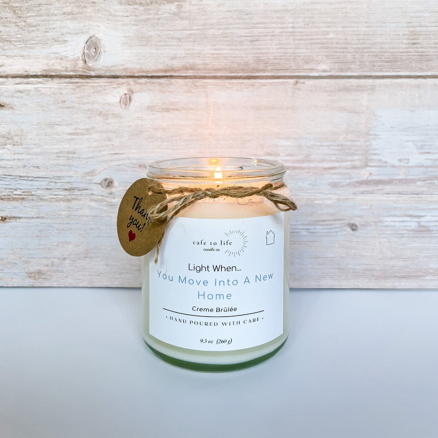 Lit candle with twine, a thank you tag, and a label that says, “Light When… You Move Into A New Home.”