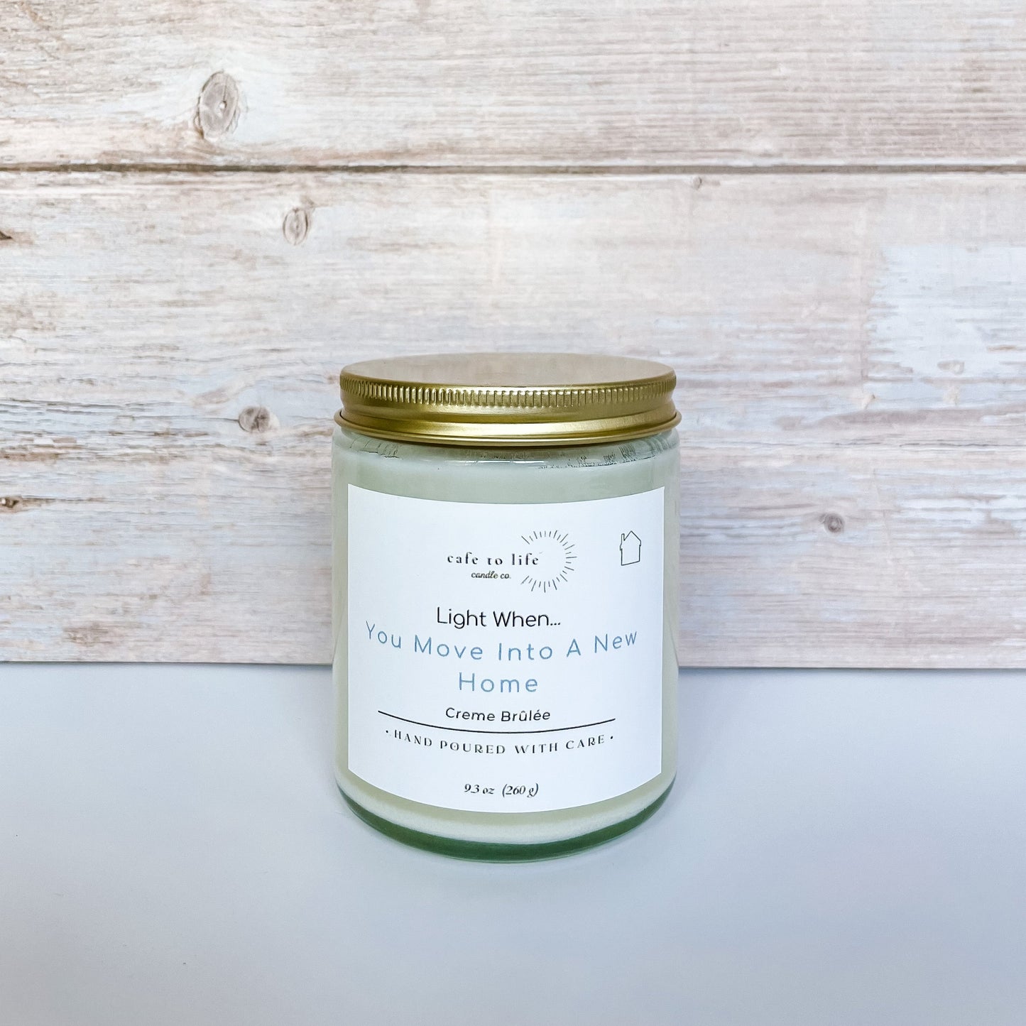 Candle with a gold top and a label that says, “Light When… You Move Into A New Home.”