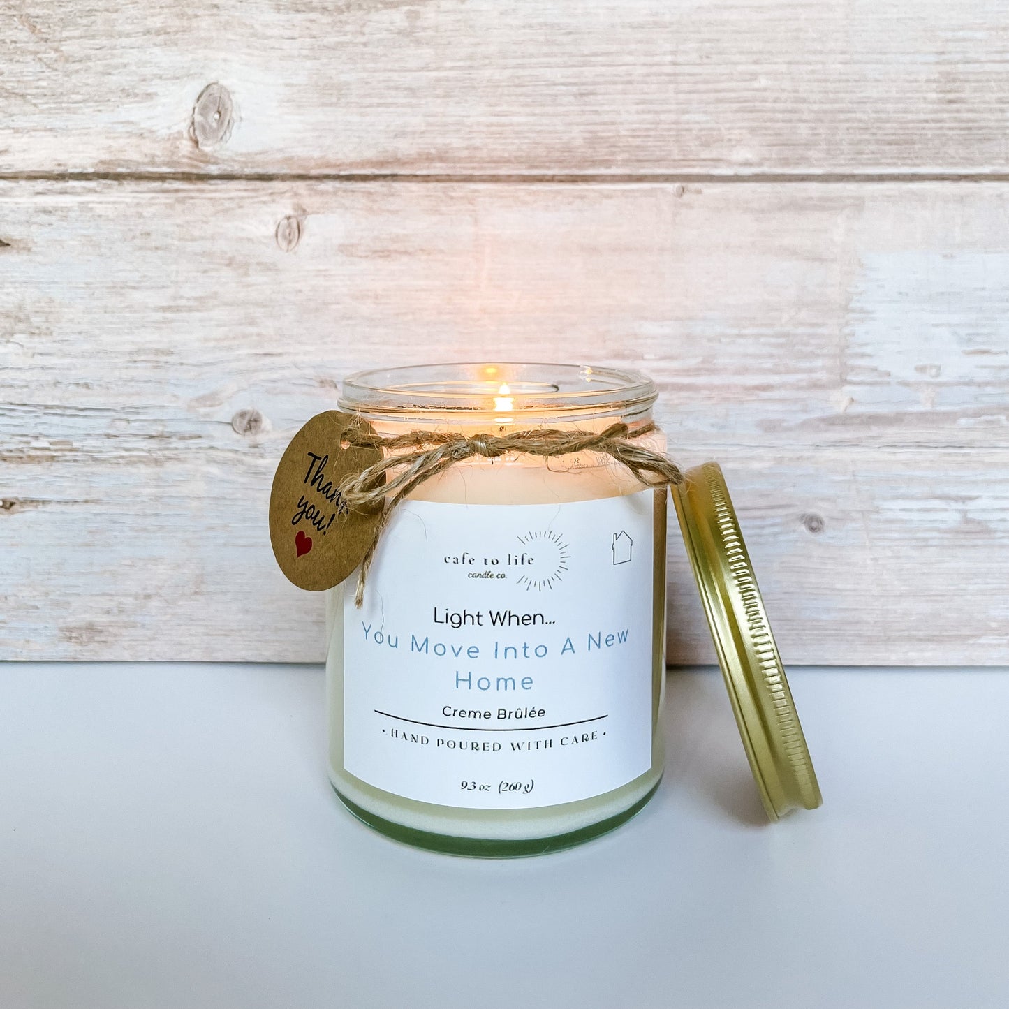 Candle with flame, twine, and a thank you card with a heart. Label says, “Light When… You Move Into A New Home.”