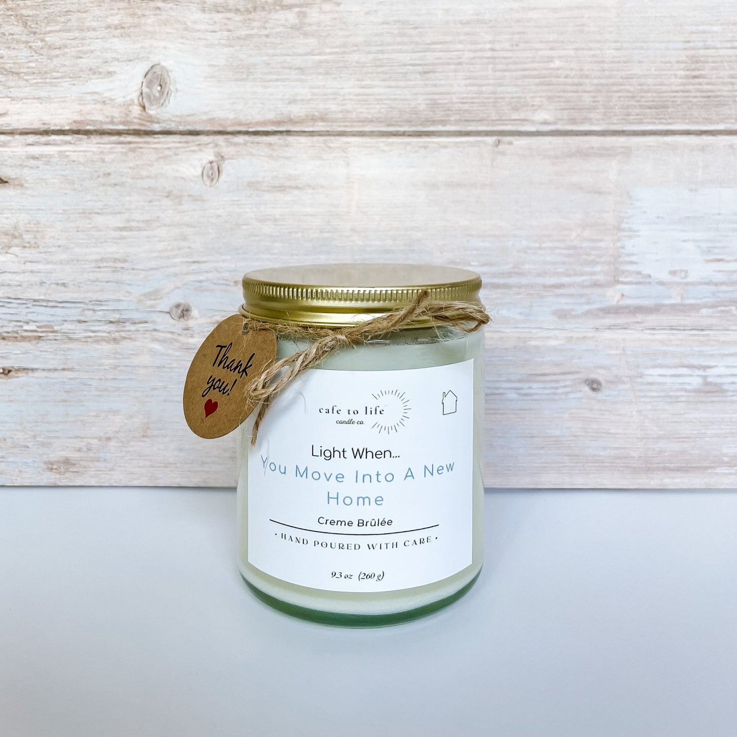 Candle with a gold top on, twine, and a thank you tag. Label on candle says, “Light When… You Move Into A New Home.”